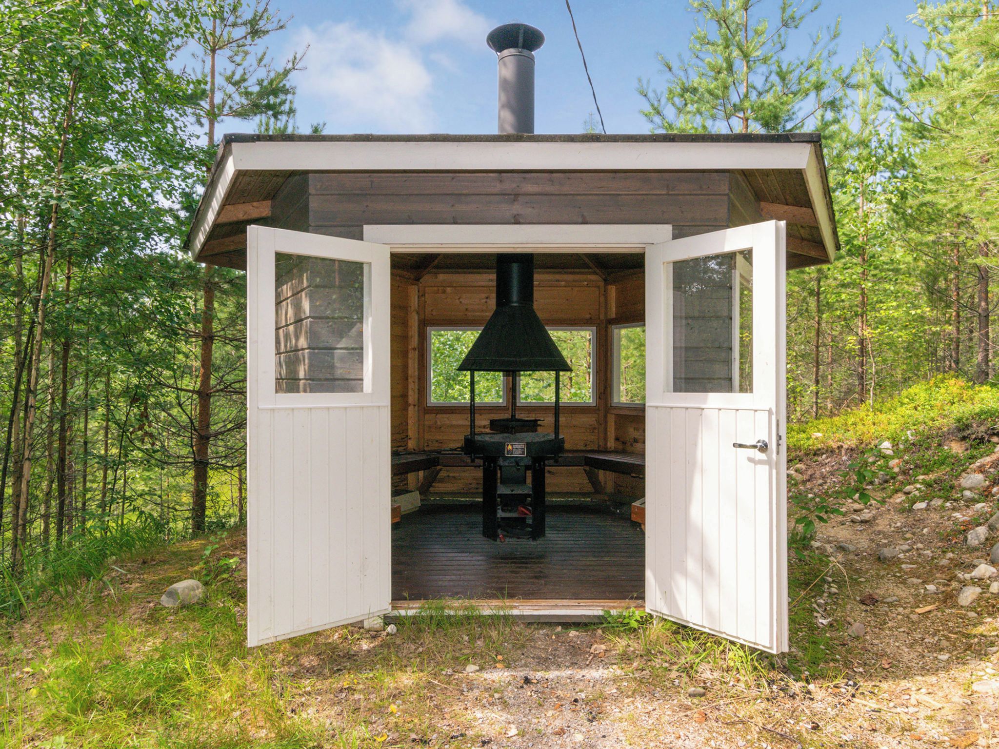 Une cabane en bois avec une porte ouverte, une cheminée et une table avec des bancs à l’intérieur.