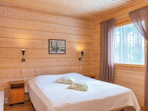 Ein Zimmer mit Holzwänden, einem Bett, zwei Wandlampen, einem Gemälde und einem Fenster mit Vorhängen.