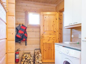 Eine kleine Küche mit Holzwänden, einer Waschmaschine, einem Feuerlöscher und einem Fenster.