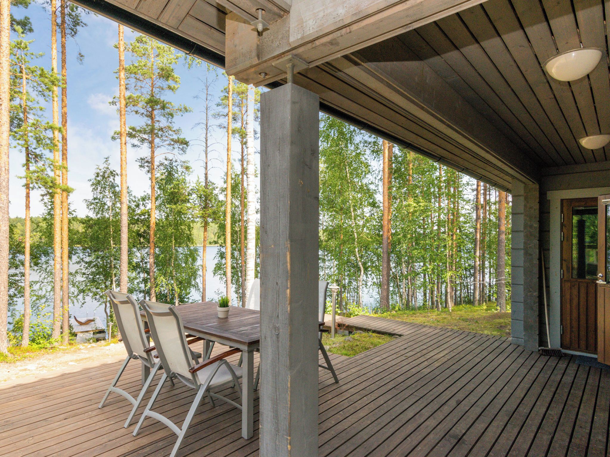 Une terrasse extérieure couverte, dotée d’une table et de chaises, qui offre une vue sur une forêt et un plan d’eau.
