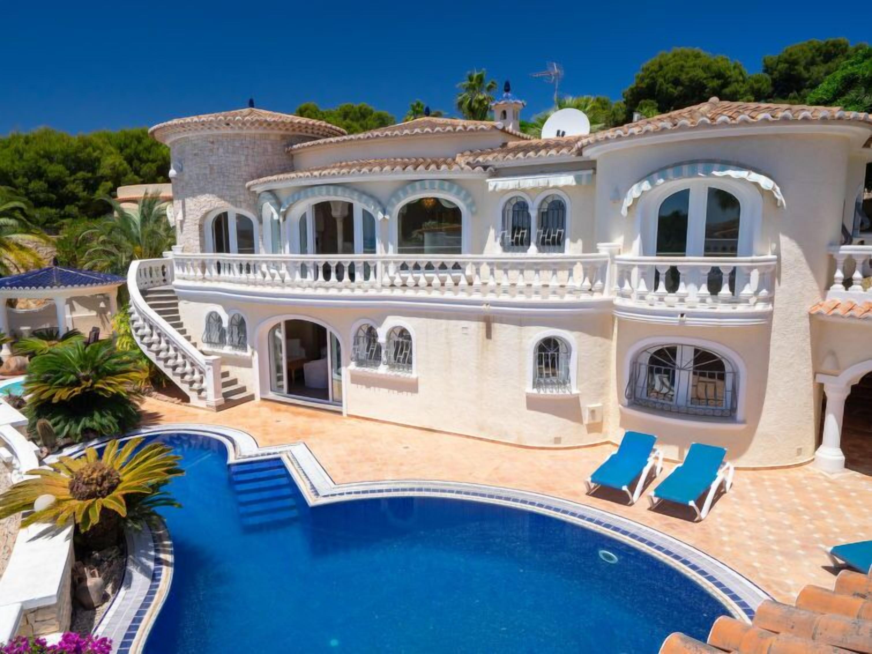 A large, white villa with a swimming pool, multiple balconies, and a staircase leading to the upper levels.
