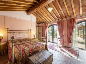 A bedroom with a bed, a wooden chest, a nightstand, and a window with curtains. - Tenuta Farneta by Interhome (Lucignano)
