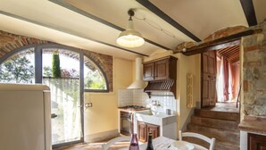 A cozy kitchen with a dining area, featuring a stone wall, wooden cabinets, and a large window. - Tenuta Farneta by Interhome (Lucignano)