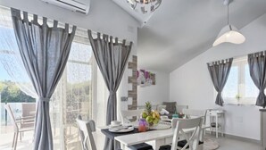 A modern dining area with white furniture and grey curtains, a small kitchen area with a dining table, and a view of the outdoors. - Apartment La Mer by Interhome (Pula)