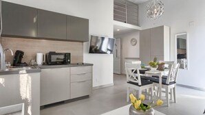 A modern kitchen with a microwave, kettle, and coffee maker. There is a dining area with a table and chairs, and a vase of flowers on the table. - Apartment La Mer by Interhome (Pula)