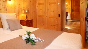 Een houten kamer met een bed, een nachtkastje, een lamp en een deur naar een andere kamer.