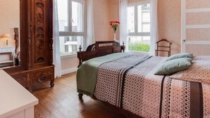 A bedroom with a large bed, a wooden dresser, a mirror, and a chandelier. - La Coloniale by Interhome (Auray)