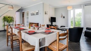 A dining area with a long table set for six, surrounded by wooden chairs. A television is mounted on the wall, and a plant is visible in the corner. - La Coloniale by Interhome (Auray)