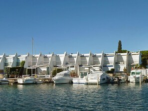 A marina with multiple boats docked in front of a row of modern, white buildings with triangular roofs. - Port Nautile by Interhome (Port Camargue)