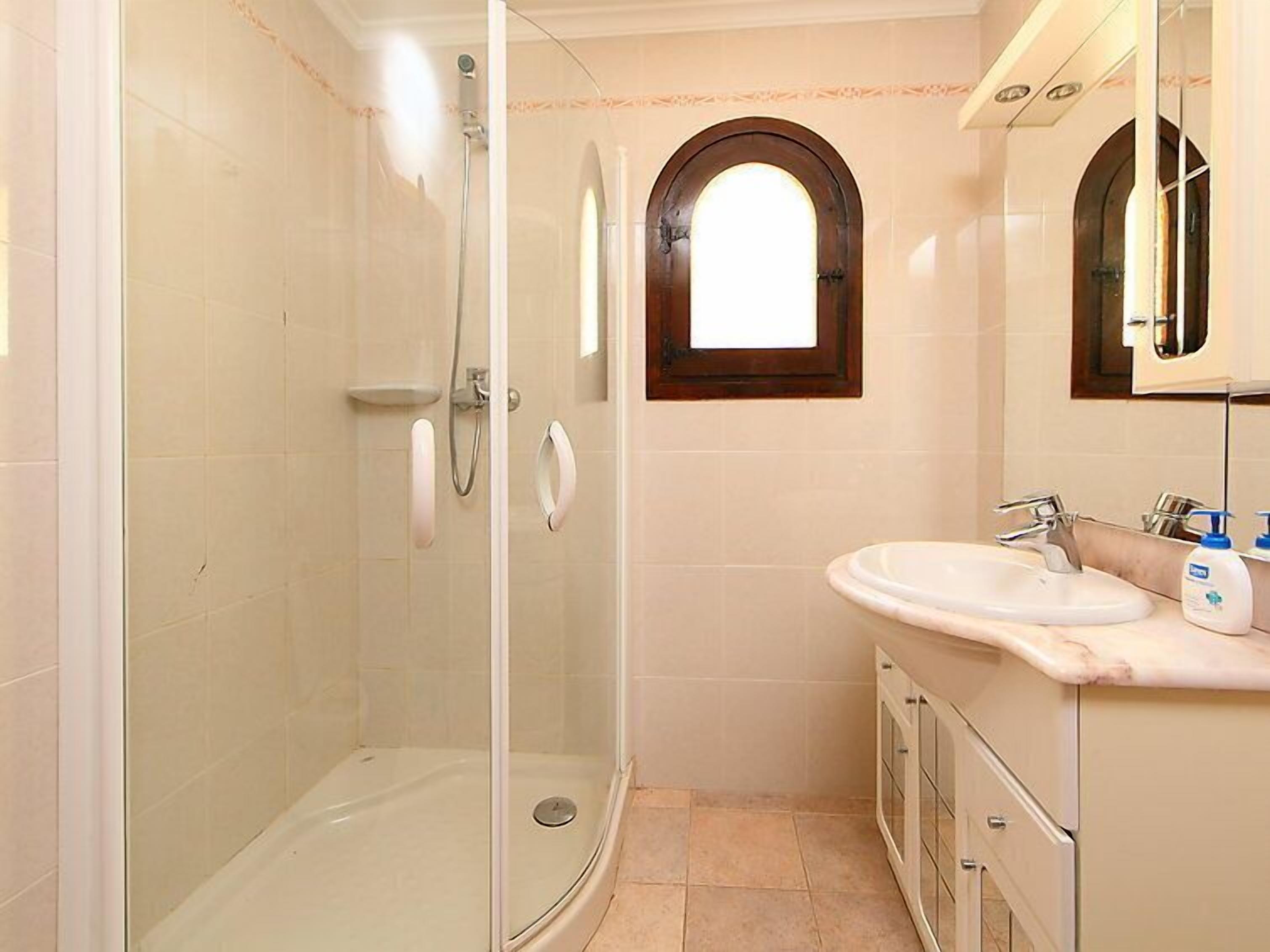 Een badkamer met een douchecabine van glas, een wastafel met een marmeren blad en een klein raam boven de spiegel.