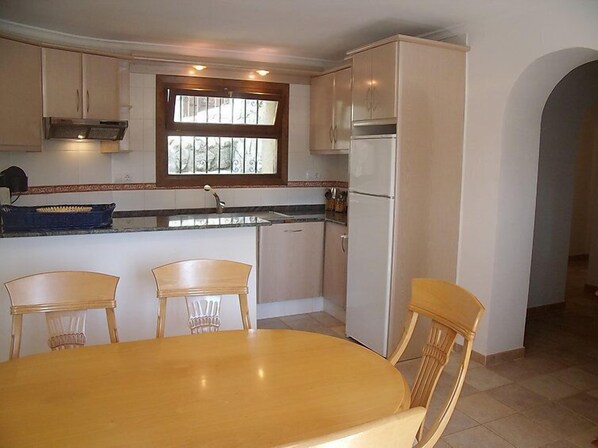 A kitchen with a dining table and chairs, a window, and a refrigerator.