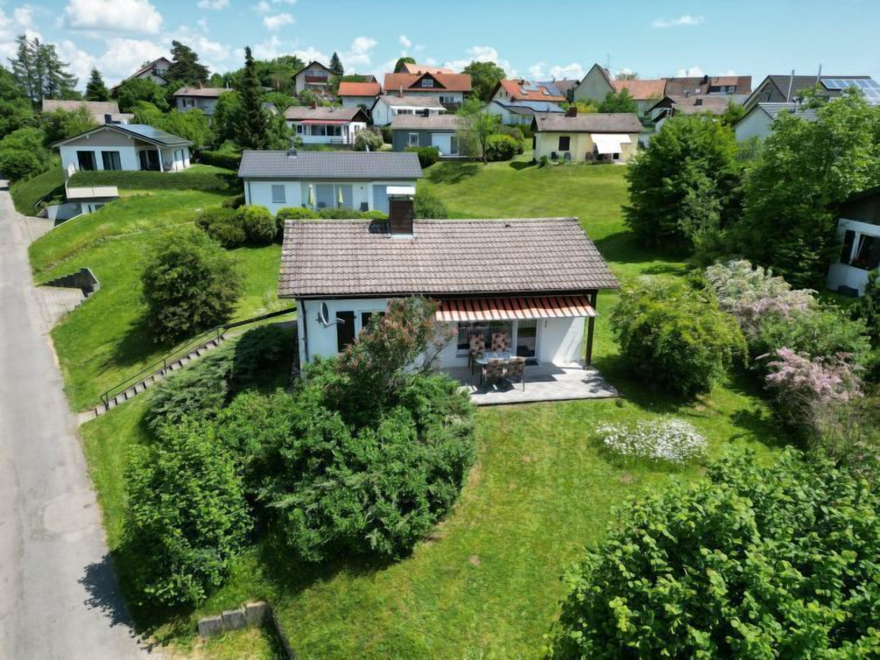 A single-story house with a tiled roof, surrounded by lush greenery and a well-maintained lawn.