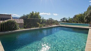 Une piscine aux eaux cristallines, bordée d’une terrasse carrelée et entourée d’une clôture en métal et d’arbres.