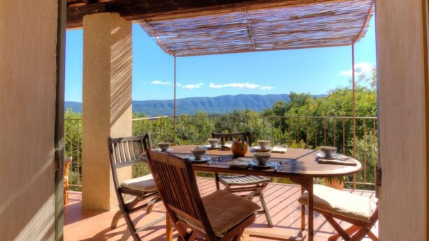 Une terrasse extérieure couverte, dotée d’une table et de chaises, qui offre une vue sur un paysage montagneux.