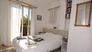 Une chambre à coucher comprenant un lit, une table de chevet, une commode, une fenêtre avec des rideaux, une bibliothèque et un miroir.