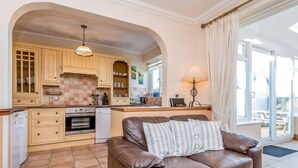 Una sala de estar acogedora con un sofá de cuero marrón, una cocina con armarios de madera y un ventanal con cortinas.