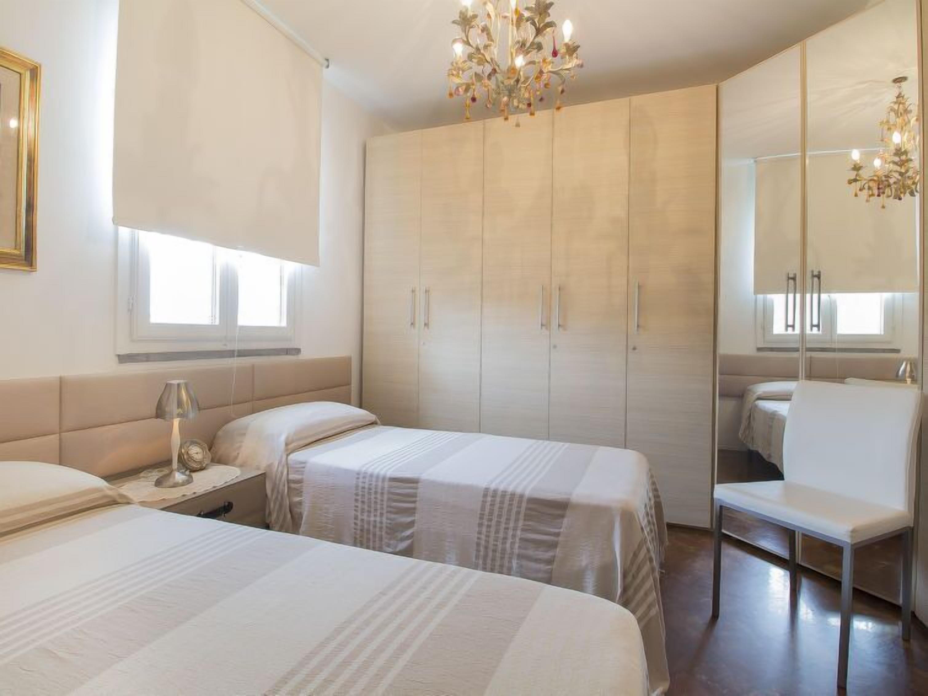 Un dormitorio con dos camas, un armario grande, una silla y una araña.