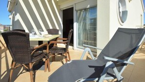 A sunlit outdoor seating area with a table and chairs, a sliding glass door, and a poolside lounge chair. - Apartment Sablić by Interhome (Pirovac)