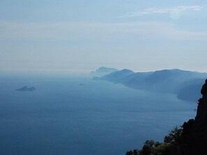 Paesaggio costiero con vista limpida sul mare e montagne in lontananza.