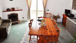 Uma sala de jantar com mesa e cadeiras de madeira, lareira e cozinha com pia e armários.