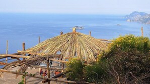 Uma construção com telhado de palha e vista para o mar e a costa rochosa.