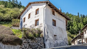 Un bâtiment à deux étages, doté d’un mur en pierre et de poutres en bois, situé sur une colline, avec des arbres en arrière-plan.