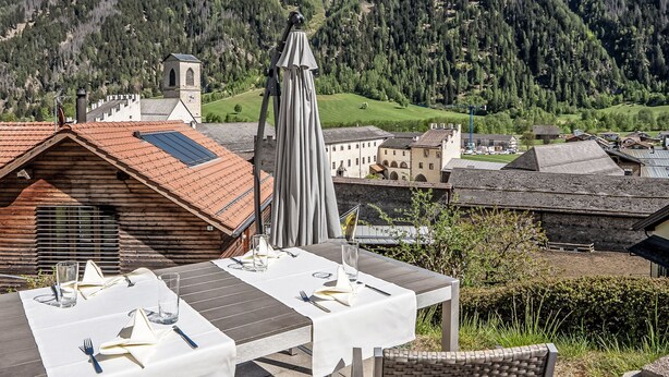 Une ville de montagne dotée d’un espace de restauration offrant une vue sur une vallée, d’une église avec un clocher et d’un paysage montagneux en toile de fond.