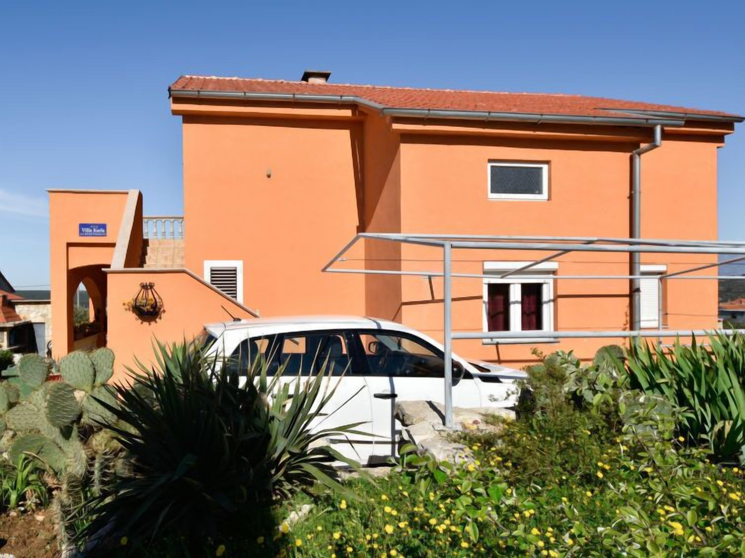 Un bâtiment doté d’un toit plat, une enseigne indiquant « Villa Kafka », et une voiture blanche garée devant.