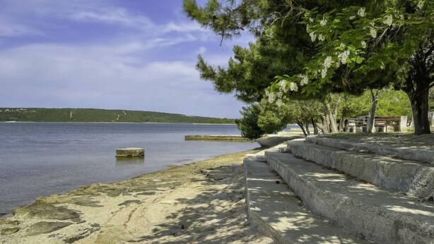 A coastal walkway with steps leading to a sandy beach, overlooking calm waters and a distant green hill. - Apartment Karla by Interhome (Novigrad (Zadar))