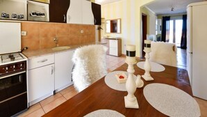A modern kitchen with white cabinets, a stove, and a dining area with a white fluffy chair and candle holders. - Apartment Karla by Interhome (Novigrad (Zadar))