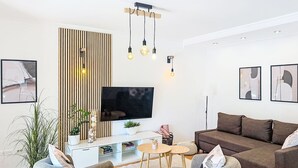 A modern living room with a flat-screen TV, a brown sofa, two grey armchairs, a wooden slat wall, and a small round table with a vase and books. - Apartment Tea by Interhome (Umag/Murine)