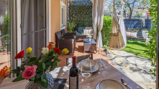 An outdoor dining area with a table set for two, a bottle of wine, and a vase of flowers. - Apartment Tea by Interhome (Umag/Murine)