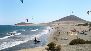 A beach with people engaging in windsurfing and kiteboarding, and a mountain in the background.