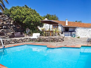 A swimming pool with a stone deck, a barbecue area, and a white building with a tiled roof. - Vacation home Pepa by Interhome (Granadilla)
