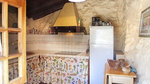 A rustic kitchen with a tiled backsplash, a wooden table, and a refrigerator.