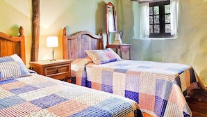 A bedroom with two beds, a nightstand, a lamp, a window with curtains, and a wooden ceiling.