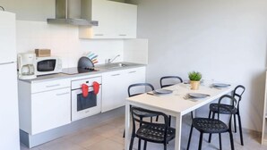 Een moderne keuken met witte kasten, een magnetron, een broodrooster en een fornuis. Er staat een eettafel met stoelen en een kleine plant in een pot.