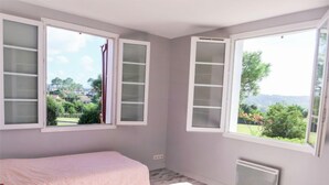 Een slaapkamer met twee bedden, grote ramen met luiken en uitzicht op groen.