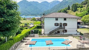 Un edificio su due piani con piscina, immerso nel verde e con montagne sullo sfondo.