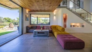Un salon moderne avec un plafond en bois, une grande fenêtre, un canapé, une table basse et un escalier.