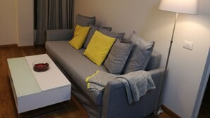 Una sala de estar moderna con un sofá gris, dos cojines amarillos, una mesa de centro blanca con un objeto rojo y una lámpara de pie.