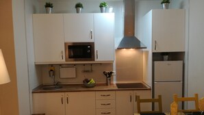 Una cocina compacta con armarios blancos, un microondas, una campana extractora de acero inoxidable, un fregadero y un pequeño comedor con una mesa y sillas.