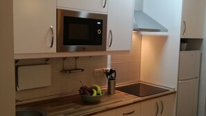 Una cocina moderna con armarios blancos, un microondas de acero inoxidable, un frutero y un horno empotrado.