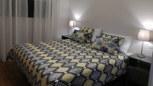Un dormitorio con colcha estampada, dos lámparas de noche, una mesita de noche y cortinas de encaje.