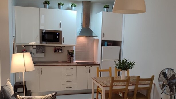 Un espacio habitable compacto con kitchenette, comedor y zona de estar con sofá y mesa.