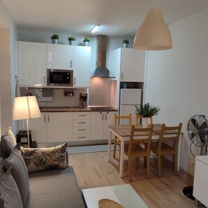 Ett kompakt bostadsutrymme med ett litet kök, en matplats och en sittgrupp med en soffa och ett bord.