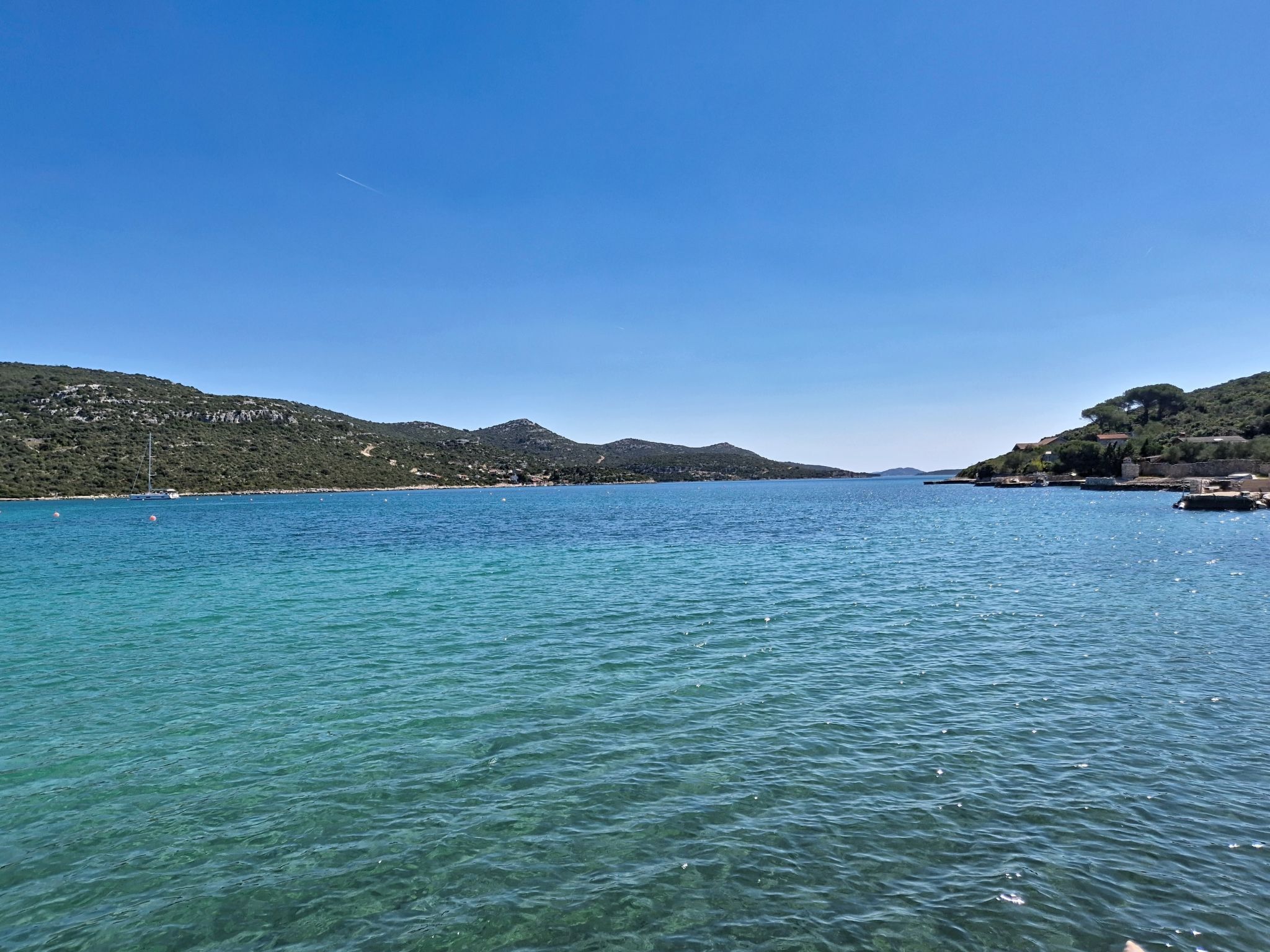 A coastal landscape with clear water, hills, and a distant shoreline.