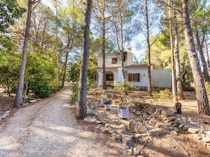 A house with a gravel driveway, surrounded by trees and a stone wall.
