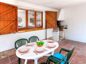 Un coin repas avec une table blanche dressée pour quatre personnes, des chaises vertes et une fenêtre dotée de volets en bois.