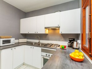 A modern kitchen with white cabinets, a stainless steel sink, a gas stove, a microwave, and a coffee maker.